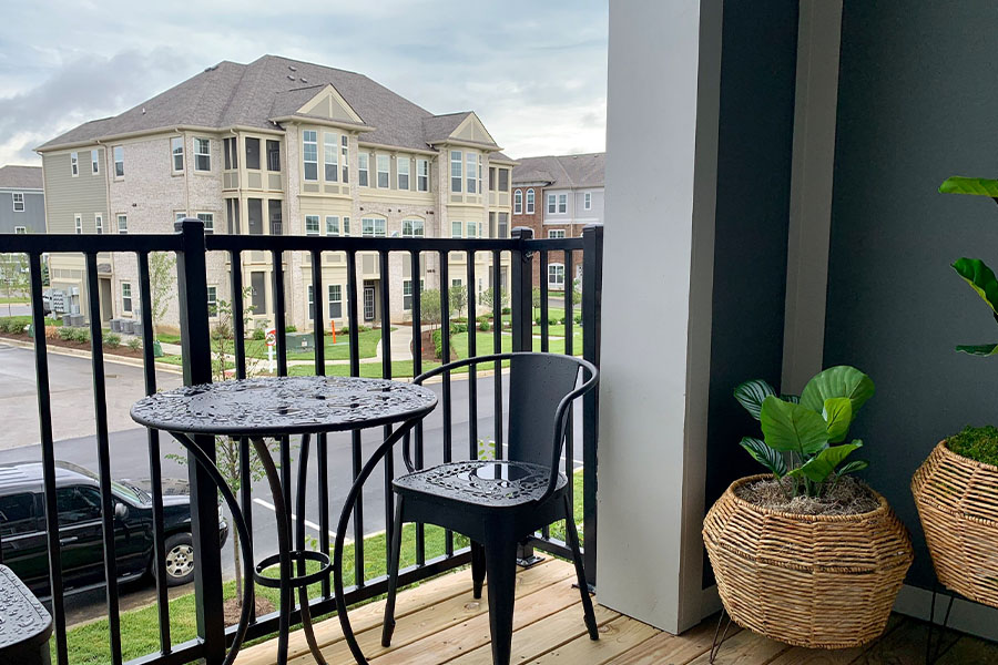 Small black patio iron table and chairs on an upper-level patio with potted plants. Located at Harmony Apartments.